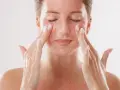 Kobieta z zamkniętymi oczami delikatnie masuje twarz, aplikując produkt z drobinkami. To może być skuteczny retinol na zaskórniki, który odnawia skórę.