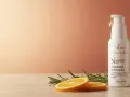 Biała buteleczka z serum na twarz, z kroplą złocistego płynu na pompce. Obok plasterki pomarańczy i gałązka rozmarynu. Idealne dla skóry, która potrzebuje odnowy dzięki kwasy aha na twarz.
