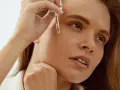 Kobieta aplikuje serum z kwasem ferulowym na twarz. Skóra wygląda na nawilżoną i promienną.