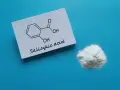 Karta z wzorem chemicznym kwasu salicylowego i jego proszkiem. Dowiedz się, jak stosować kwas salicylowy.