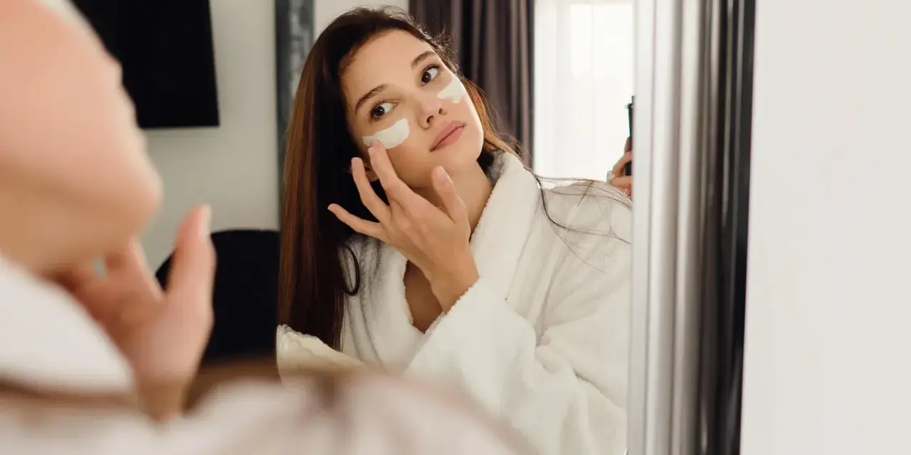 Kobieta w szlafroku nakłada krem pod oczy. Czy retinol to kwas? To pytanie nurtuje wiele osób dbających o cerę.