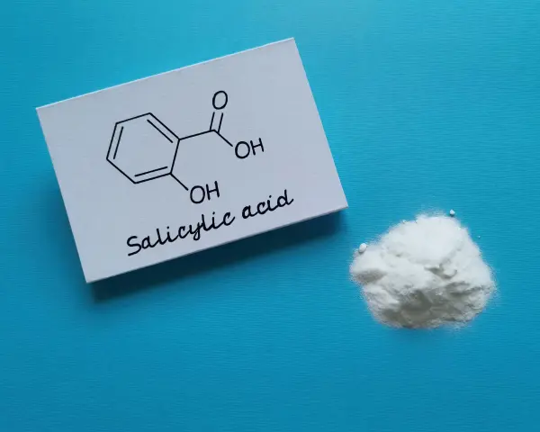 Karta z wzorem chemicznym kwasu salicylowego i jego proszkiem. Dowiedz się, jak stosować kwas salicylowy.